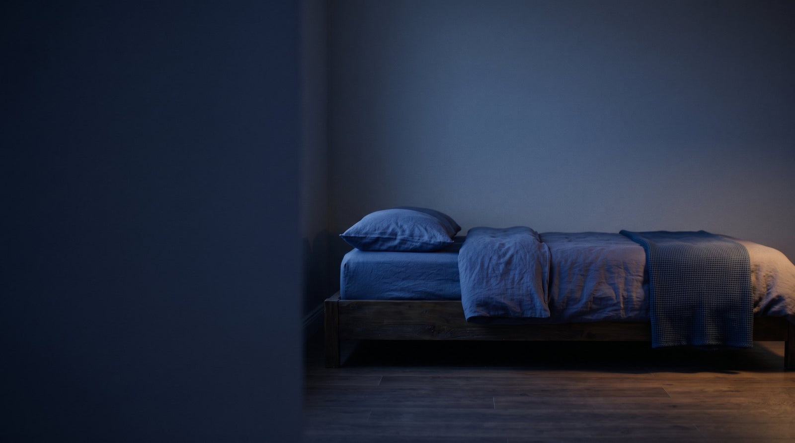 A calm bedroom at dusk with a bed dressed in soft indigo linen